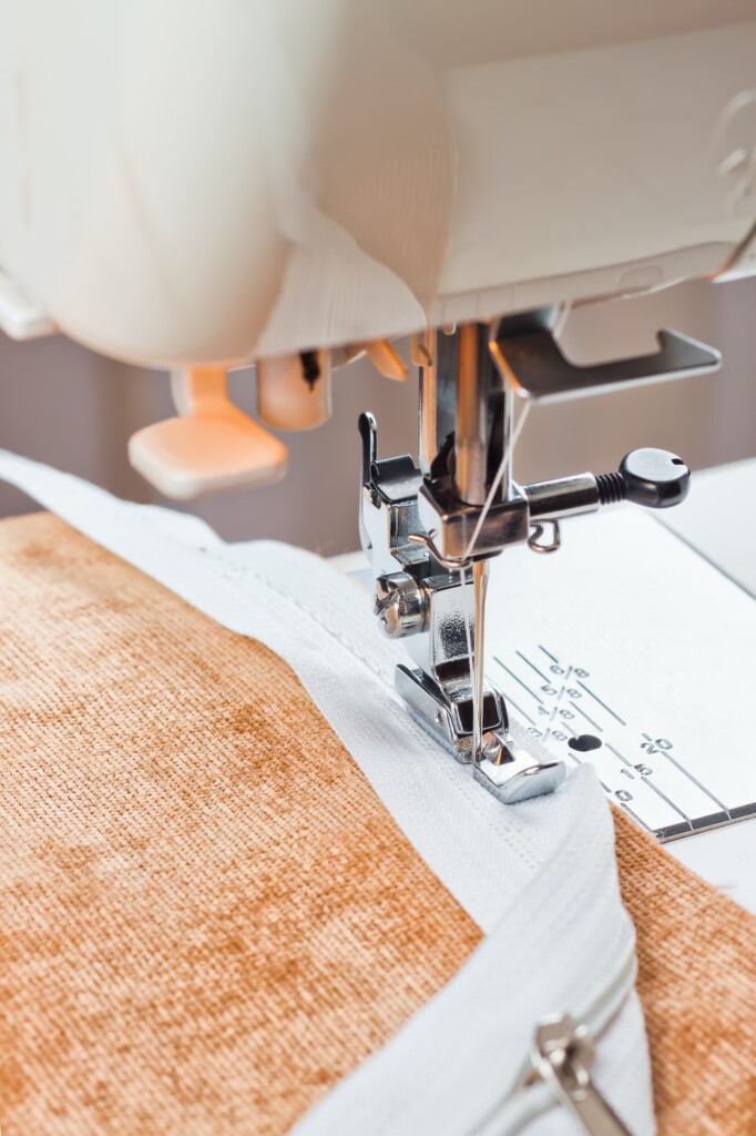 Modern sewing machine sews on the zipper on beige item of clothing. sewing process